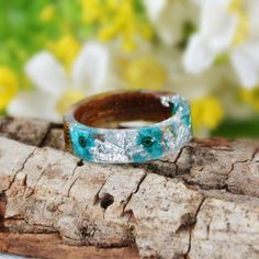 a wooden ring sitting on top of a piece of wood next to white and blue flowers