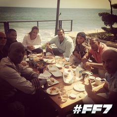 a group of people sitting around a table with food on it near the ocean and beach