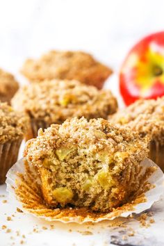 muffins with crumbs and an apple in the background on a white surface