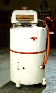 a white machine sitting in a garage next to a red and white hose connected to it