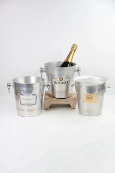 three buckets with champagne bottles in them on a wooden stand next to two ice buckets