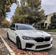 a white car parked on the side of a road in front of some trees and leaves