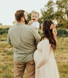 a man and woman are holding a baby in their arms while standing in the grass