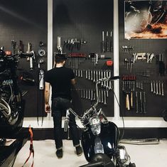 a man standing next to a motorcycle in front of a wall with tools on it