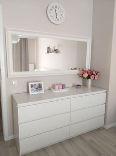 there is a clock on the wall above a dresser with flowers and candles in front of it