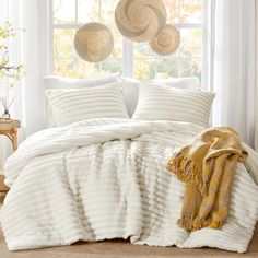 a white bed in a bedroom next to a window with two baskets hanging above it