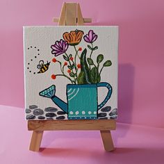 an easel with a painting on it and flowers in a watering can next to a bee