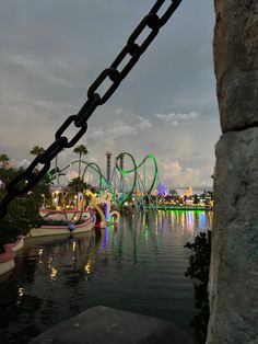 the amusement park is lit up at night with lights reflecting in the water and people riding on roller coasters