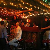 a group of people sitting at a bar with lights on the ceiling and chairs around them