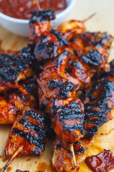 several skewers of barbecue chicken on a cutting board with ketchup in a bowl