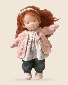 a doll with long red hair wearing a pink sweater and jeans, standing on a white background