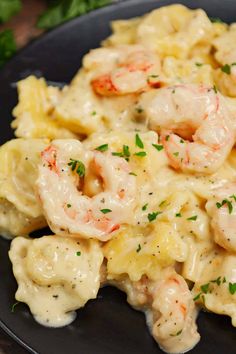 a black plate topped with pasta covered in shrimp and cheese sauce, garnished with parsley