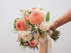 a bridal bouquet being held by a woman's hand with white and peach flowers