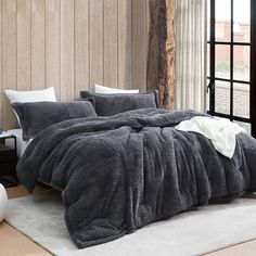 a bedroom with a large bed covered in grey comforter and pillows, along with a white rug on the floor