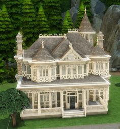 a large white victorian style house in the middle of some green grass and trees with rocks behind it