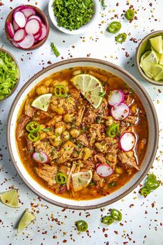 a bowl filled with meat and vegetables on top of a white table next to limes