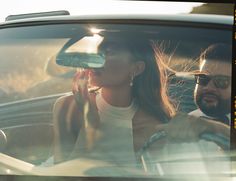 a woman talking on her cell phone while sitting in a car with another man behind her