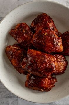 a white bowl filled with cooked meat on top of a table