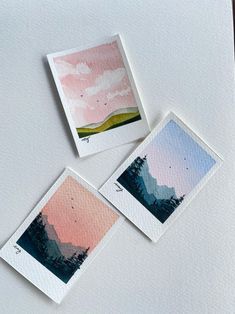 three watercolor paintings are shown on top of a white surface, one is pink and the other is blue