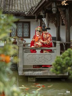 two people dressed in traditional chinese garb sitting on a bridge over a body of water