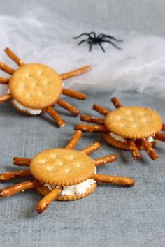 three crackers with cream cheese and spider legs on them sitting in front of a white cloth