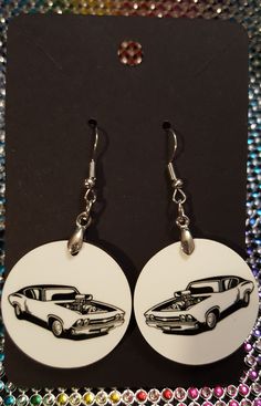 pair of white earrings with black and silver car design on them, sitting on top of colorful sequins