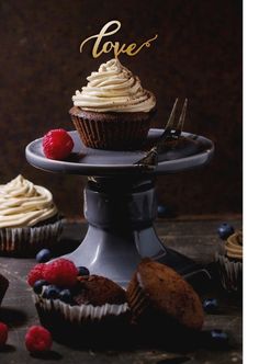 two cupcakes with white frosting and raspberries on a cake stand