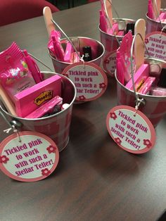 several buckets with pink items in them sitting on a wooden table and tags attached to them