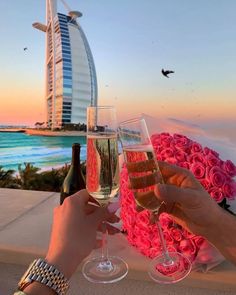 two people toasting with wine glasses in front of the burj hotel and pink roses