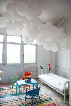 a room with a bed, table and chairs in it that has paper lanterns hanging from the ceiling