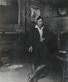 an old black and white photo of a woman standing in a room with a fireplace