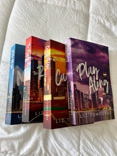 three paperback books sitting on top of a white bed sheet in front of a cityscape