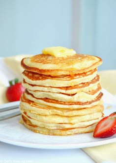 a stack of pancakes sitting on top of a white plate next to strawberries and a knife