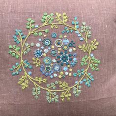 an embroidered pillow with flowers and leaves in the center on a brown linen cushion cover