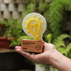 a hand holding a rubber stamp with a lightbulb on it in front of some plants