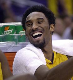 a man with a towel around his neck smiles as he sits in the stands at a basketball game