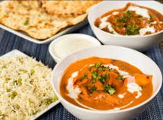 three bowls filled with different types of food on top of a blue place mat next to rice and pita bread