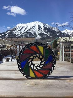 a multicolored stained glass piece sitting on top of a wooden table in front of a snow covered mountain