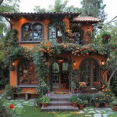 an orange house with lots of potted plants and flowers on the front porch, surrounded by greenery