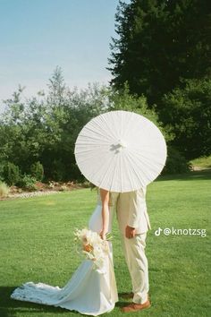 a bride and groom holding an umbrella in the grass