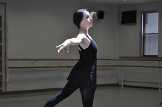 a ballerina in a black leotard with her arms outstretched