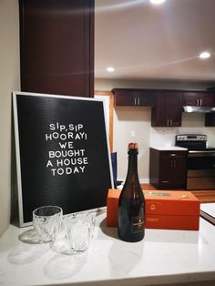 a bottle of beer sitting on top of a counter next to two glasses and a sign