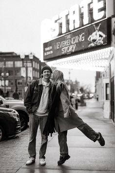 black and white photograph of two people walking down the sidewalk in front of a theater