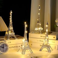 three lit up eiffel tower figurines sitting next to each other on top of books