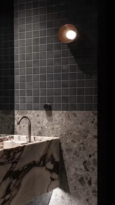 a bathroom sink sitting under a light next to a tiled wall