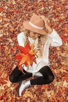 a woman sitting on the ground with leaves in front of her and wearing a hat