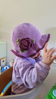 a small child wearing a purple crocheted hat with flowers on it's brim