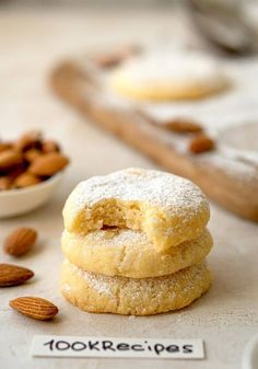 three almond cookies stacked on top of each other next to a small bowl of nuts