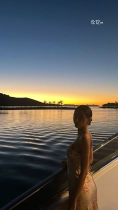 a woman is standing on the deck of a boat at sunset, looking out over the water