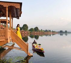 a woman in a yellow dress standing on a dock next to a boat with flowers